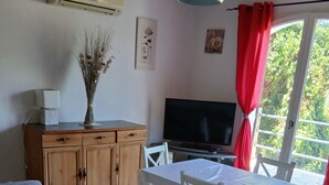 Una sala de estar con sofá, una mesa de comedor con sillas, televisor y ventana con cortinas.