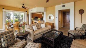 A spacious living area with a sofa, chairs, a coffee table, and a dining set. There is a kitchen in the background and a door leading to another room. - Kumulani I-1: Breathtaking Ocean Views w/ Wrap Around Lanai, Pool & AC (Kamuela)