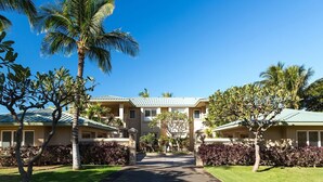 A two-story building with a central entrance, surrounded by palm trees and well-maintained lawns. - Kumulani I-1: Breathtaking Ocean Views w/ Wrap Around Lanai, Pool & AC (Kamuela)