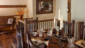 Un comedor con una mesa de madera dispuesta para cuatro, con una decoración rústica que incluye piñas y velas.