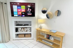 A living room with a flat-screen TV displaying streaming services, a white console with storage, a wooden console table with decorative items, and wall-mounted decorative plates.