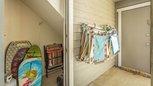 A room with a door, a wall-mounted rack with various items, and a colorful turtle surfboard. - Gulf Views · Steps to Beach & Beachfront Pool (Port St. Joe)
