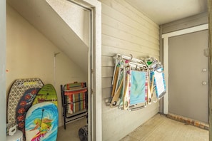 Une pièce avec une porte, un étagère fixée au mur où sont rangés divers objets, et une planche de surf colorée en forme de tortue.