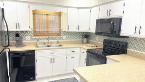 A kitchen with white cabinets, a microwave, a stove, a dishwasher, and a window with blinds. - Gulf Views · Steps to Beach & Beachfront Pool (Port St. Joe)
