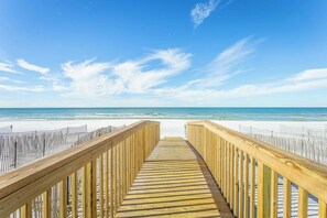 A wooden boardwalk leading to a beach with white sand and a clear blue sky.