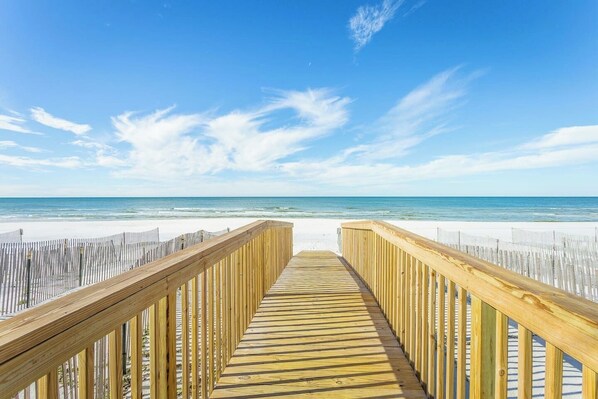 Un muelle de madera que conduce a una playa de arena blanca y un cielo azul despejado.