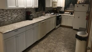A kitchen with white cabinets, a stove, a sink, and a trash can. - Quiet Beautiful Cabin in the Woods (Fall Brook)
