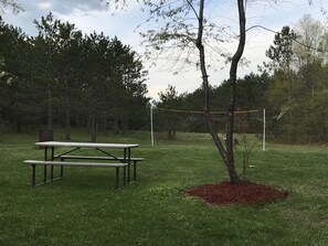 Ett picknickbord i ett grönområde med träd, och i bakgrunden syns ett nät för volleyboll.