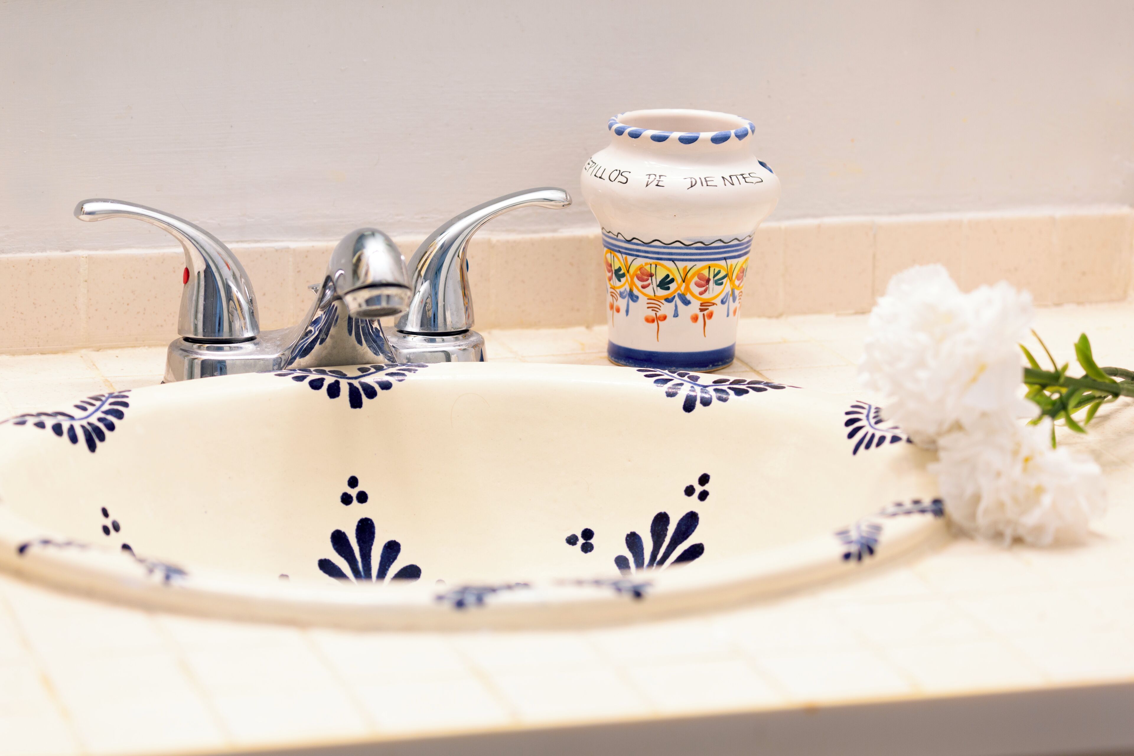 Een badkamermeubel met een witte keramieken wasbak met blauwe bloemmotieven, een chromen kraan en een decoratieve keramische beker met een blauwe rand en bloemendesign.