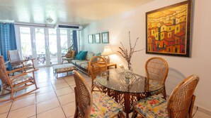 Un coin repas avec des chaises en osier et une table en verre, un canapé avec des coussins et un tableau au mur.