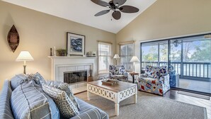 A living room with a fireplace, a ceiling fan, and a large window.