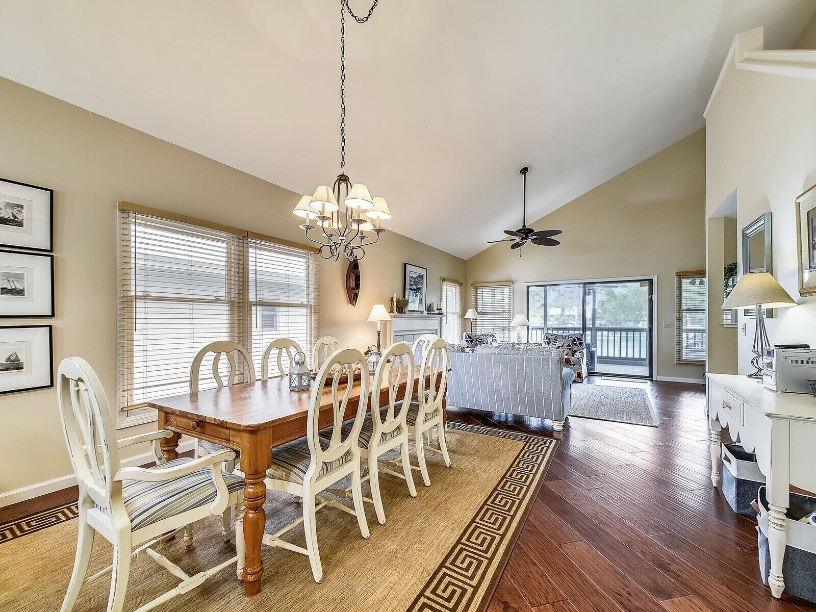A dining area with a wooden table and white chairs, a chandelier, and a ceiling fan.