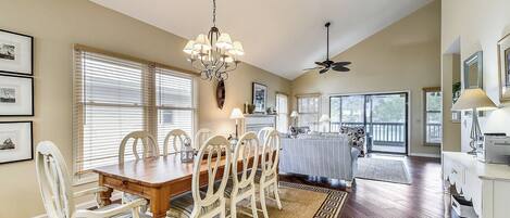 A dining area with a wooden table and white chairs, a chandelier, and a ceiling fan.