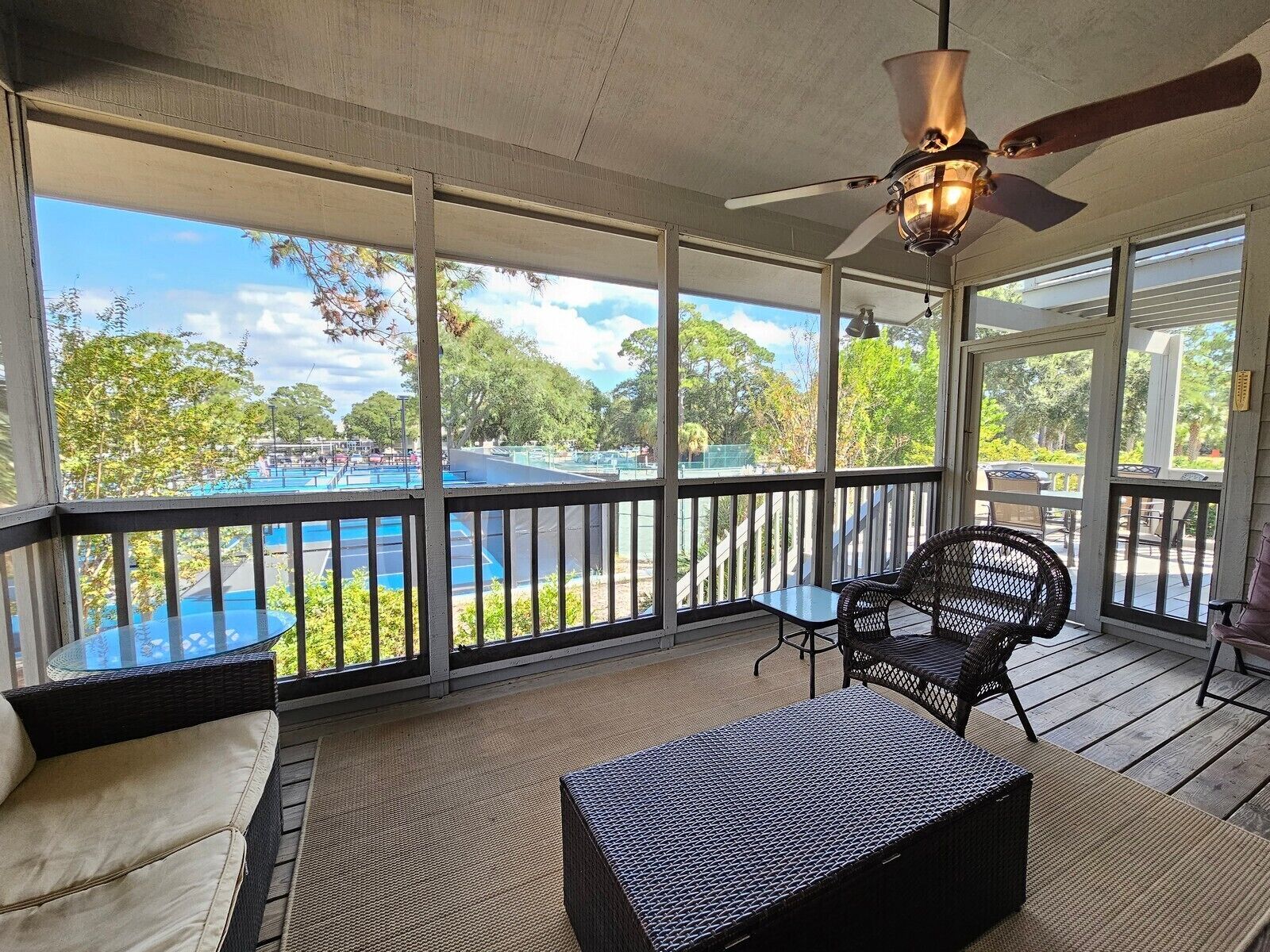 A covered outdoor area with a view of a pool, wicker furniture, and a ceiling fan.