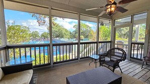 A covered outdoor area with a view of a pool, wicker furniture, and a ceiling fan.