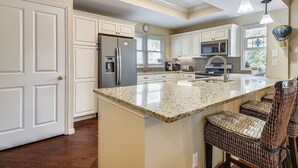 A spacious kitchen with white cabinetry, a granite countertop, and a central island with bar stools.