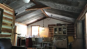 A rustic kitchen with a dining area, wooden ceiling beams, and a refrigerator.