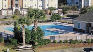 En bostadsbyggnad med en swimmingpool, omgiven av palmer och ett inhägnat område.