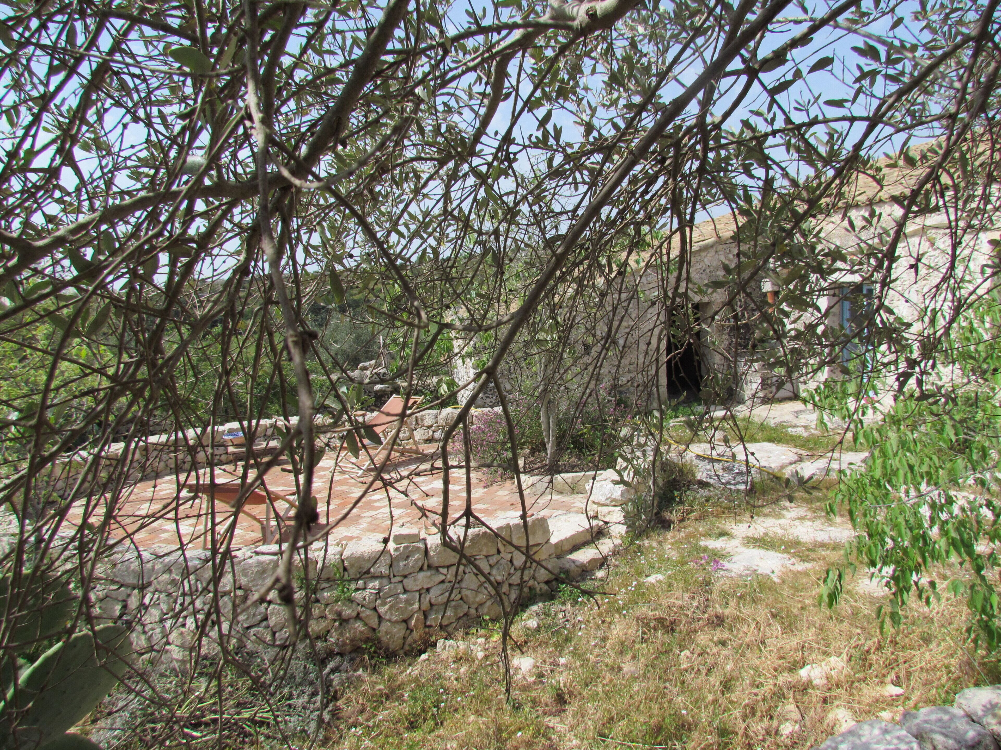 A stone pathway leading to a rustic building with a stone wall and a tiled roof.