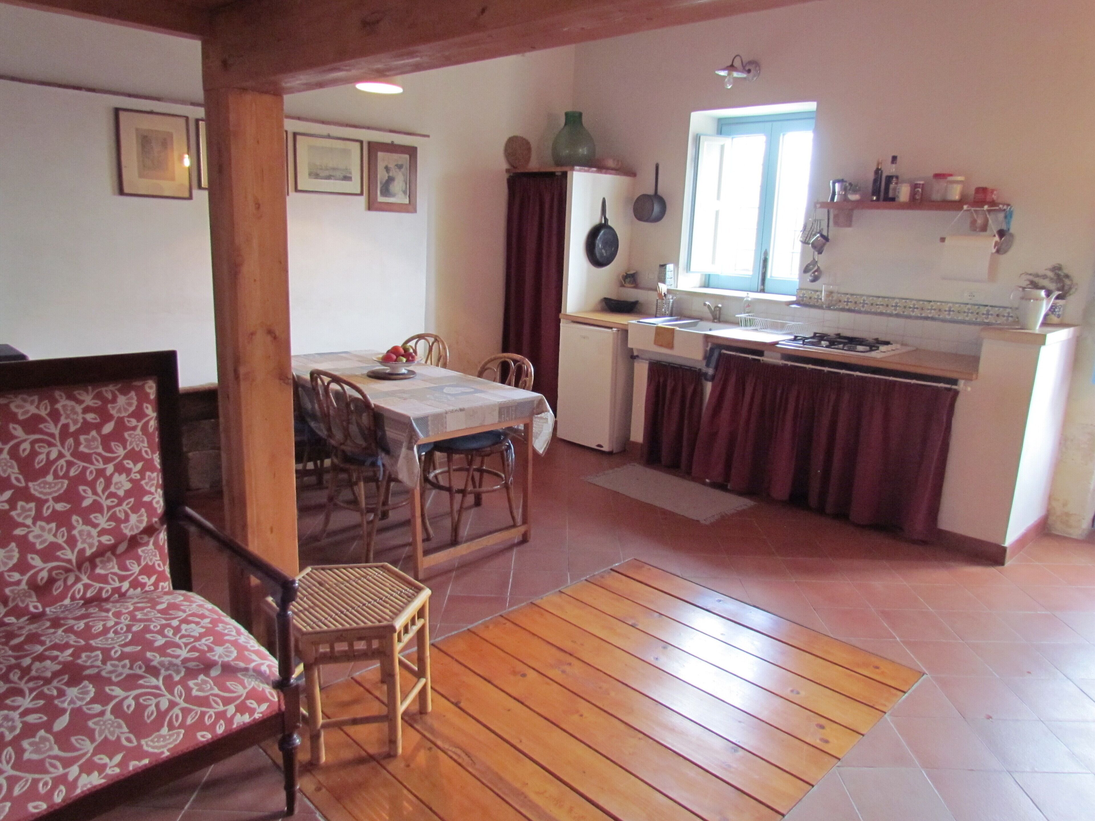 A cozy kitchen with a dining area, wooden flooring, and a red sofa.