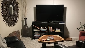 Ett vardagsrum med en svart lädersoffa, ett soffbord i trä, en bokhylla och en tv med platt skärm.