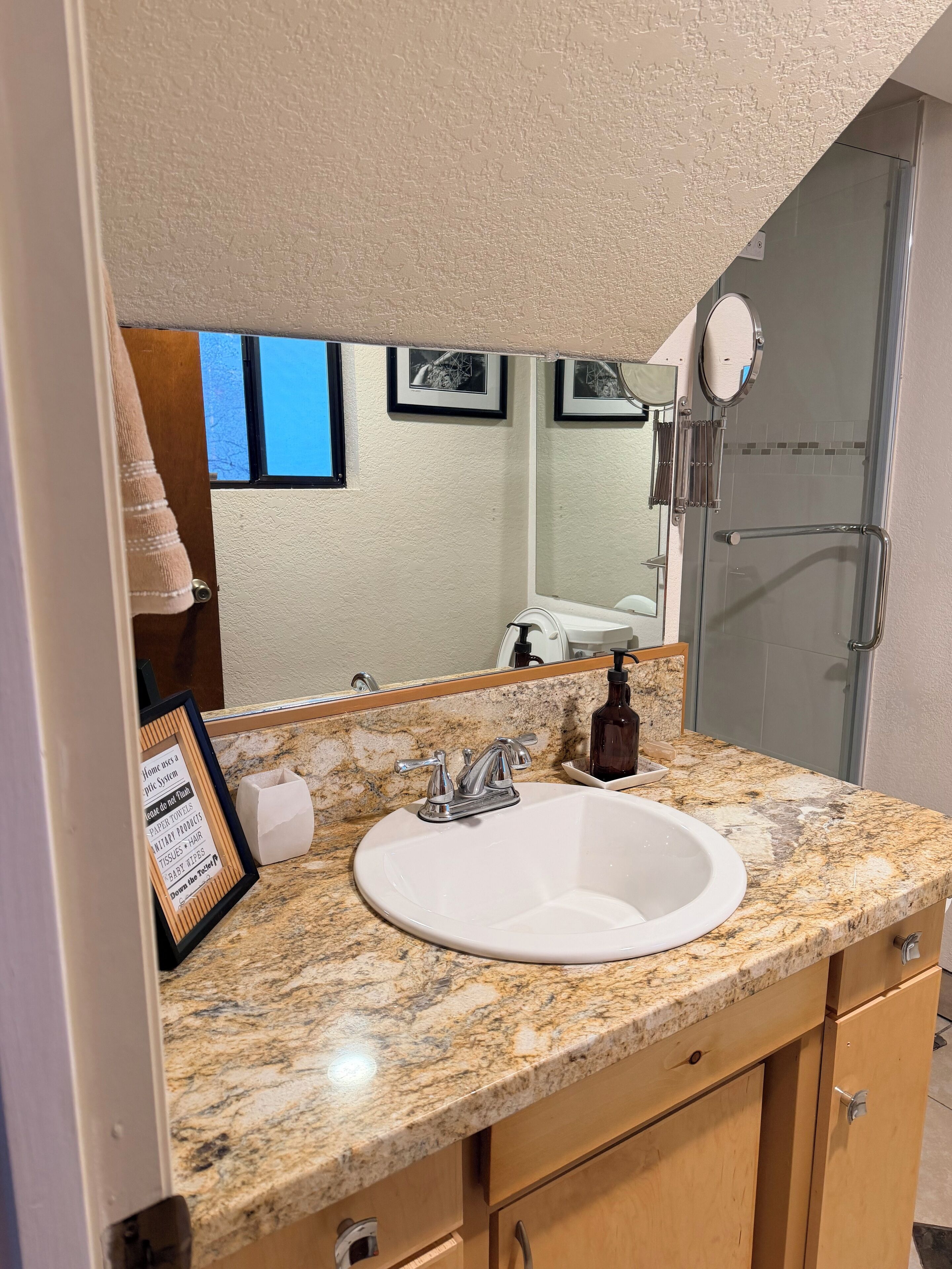 A bathroom with a granite countertop, a white sink, a mirror, and a shower area.