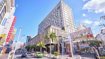 Un edificio moderno con un llamativo frente de vidrio, un restaurante visible llamado "Steak House" en la planta baja, y un cielo azul despejado.