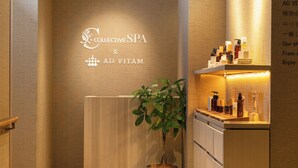 A spa reception area with a wooden reception desk, a potted plant, and a shelf with various spa products. - Hotel Collective (Naha)