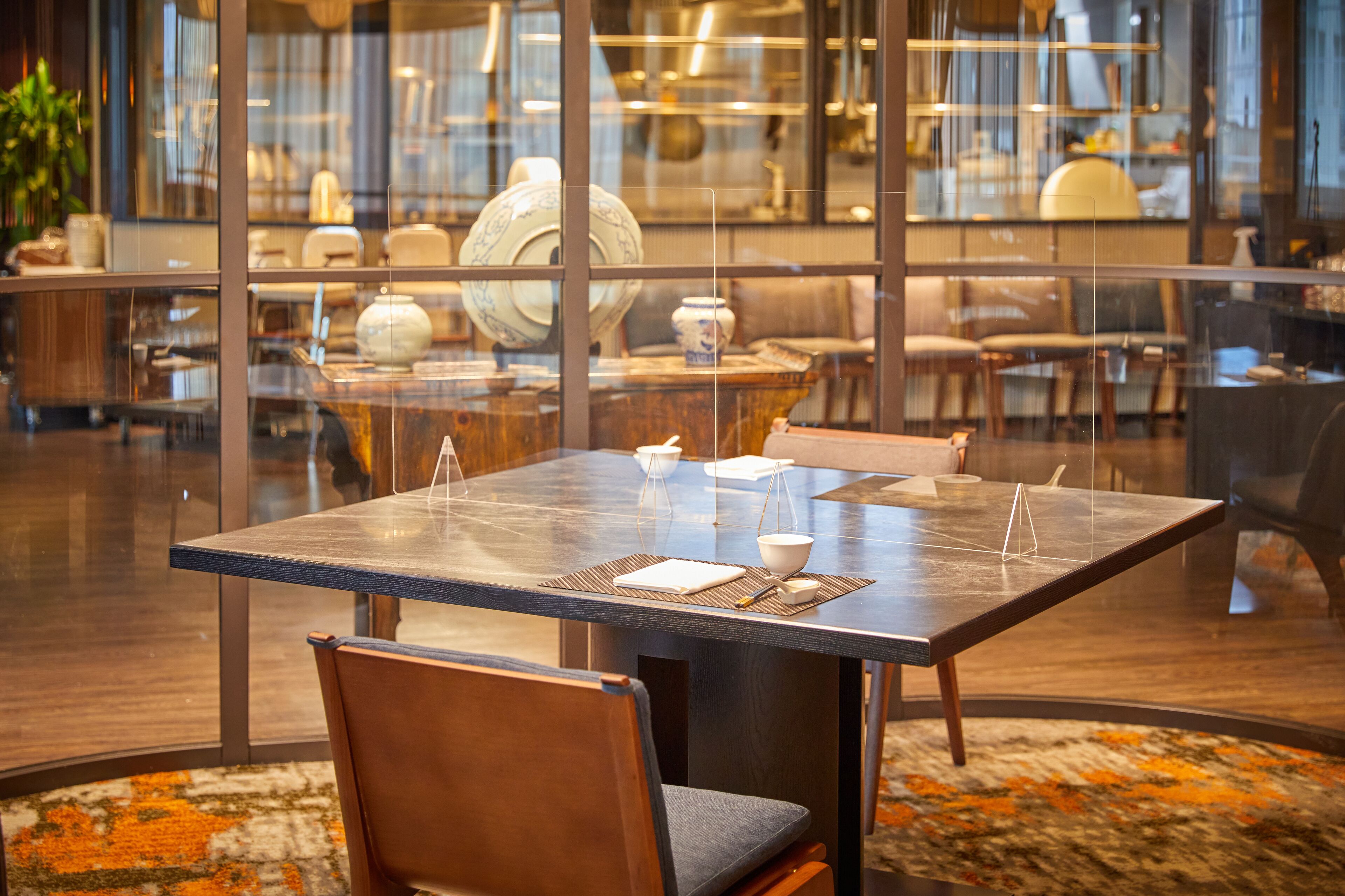 A modern dining area with a glass partition, a marble table, and a patterned rug.