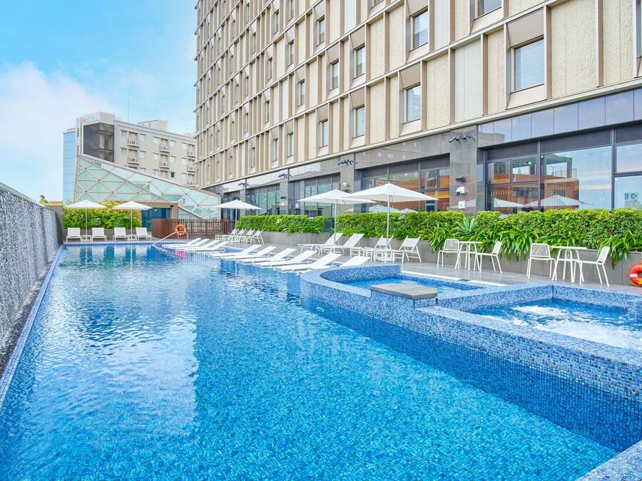 A modern hotel pool with multiple sections, lounge chairs, and umbrellas.
