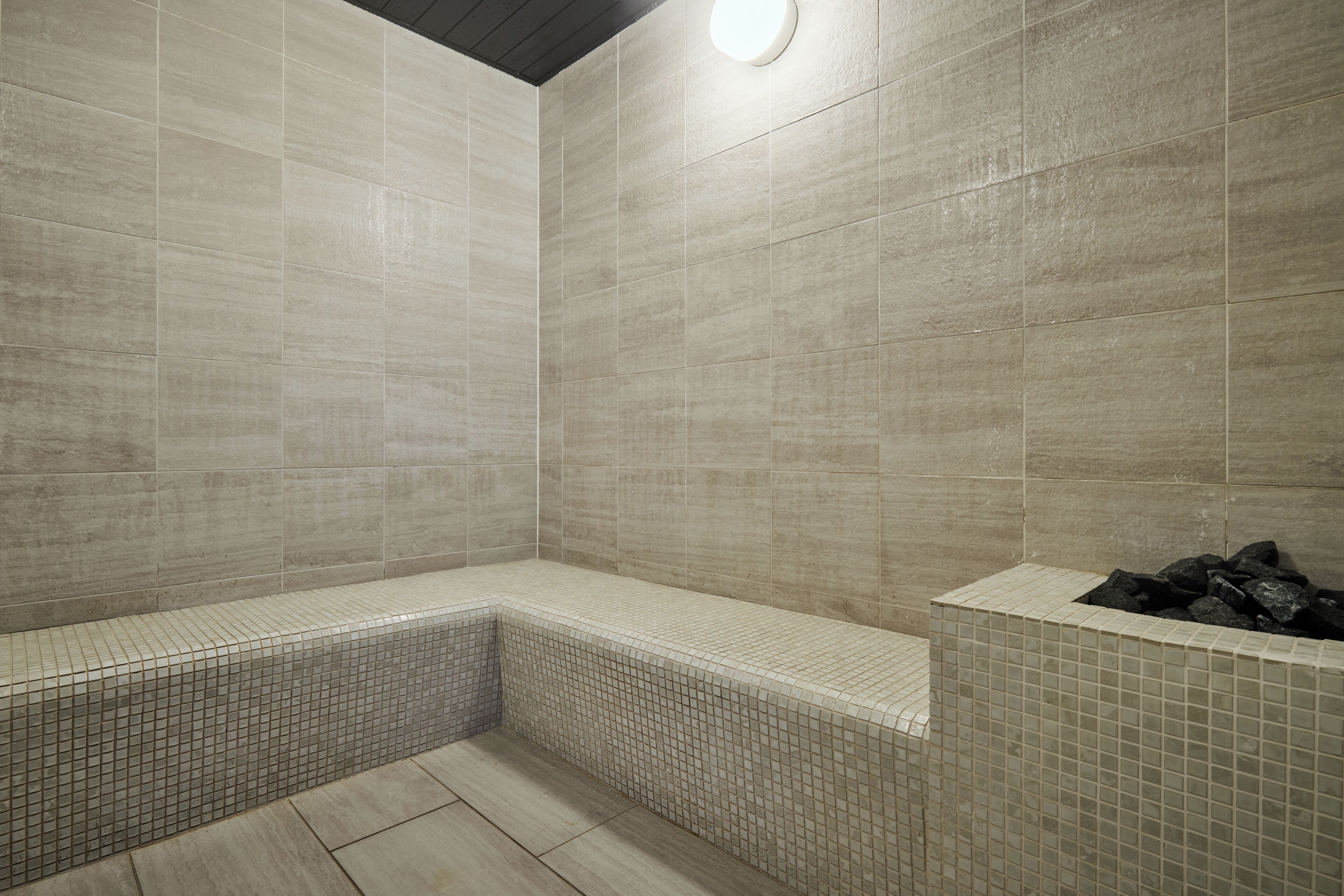 A bathroom with beige tiled walls, a bench, and a tiled floor.