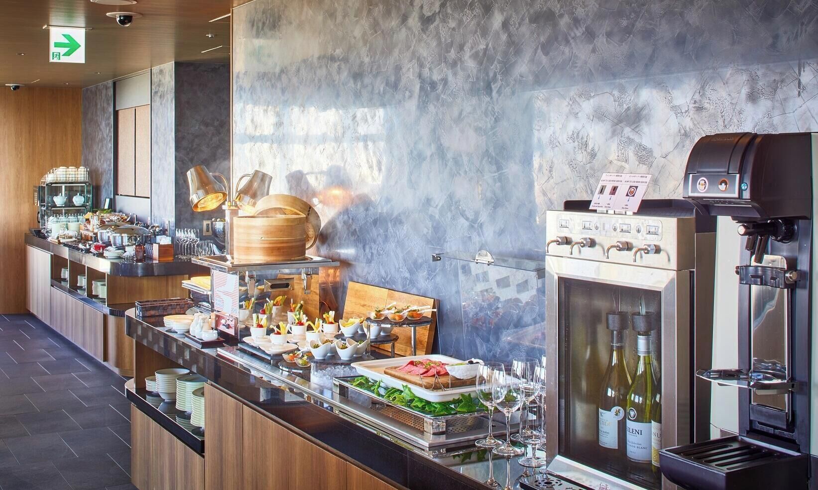 A modern buffet setup with various food stations, a wine cooler, and a coffee machine.