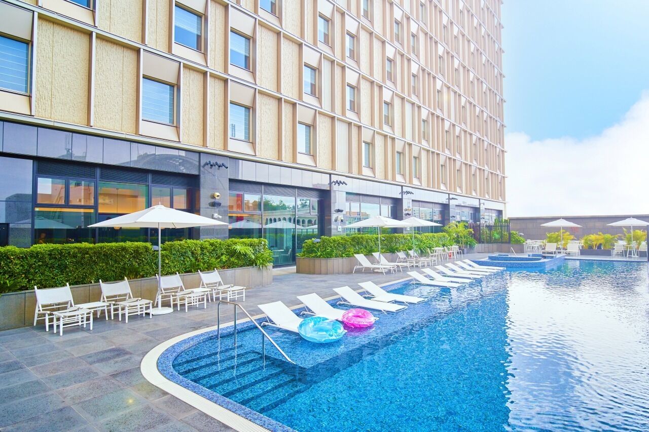 A hotel with a swimming pool, lounge chairs, and umbrellas.