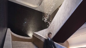 A modern staircase with a chandelier, marble steps, and a dark wall. - Hotel Collective (Naha)