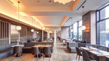 Un restaurant spacieux avec de hauts plafonds, un éclairage moderne et de grandes fenêtres offrant une vue sur la ville.