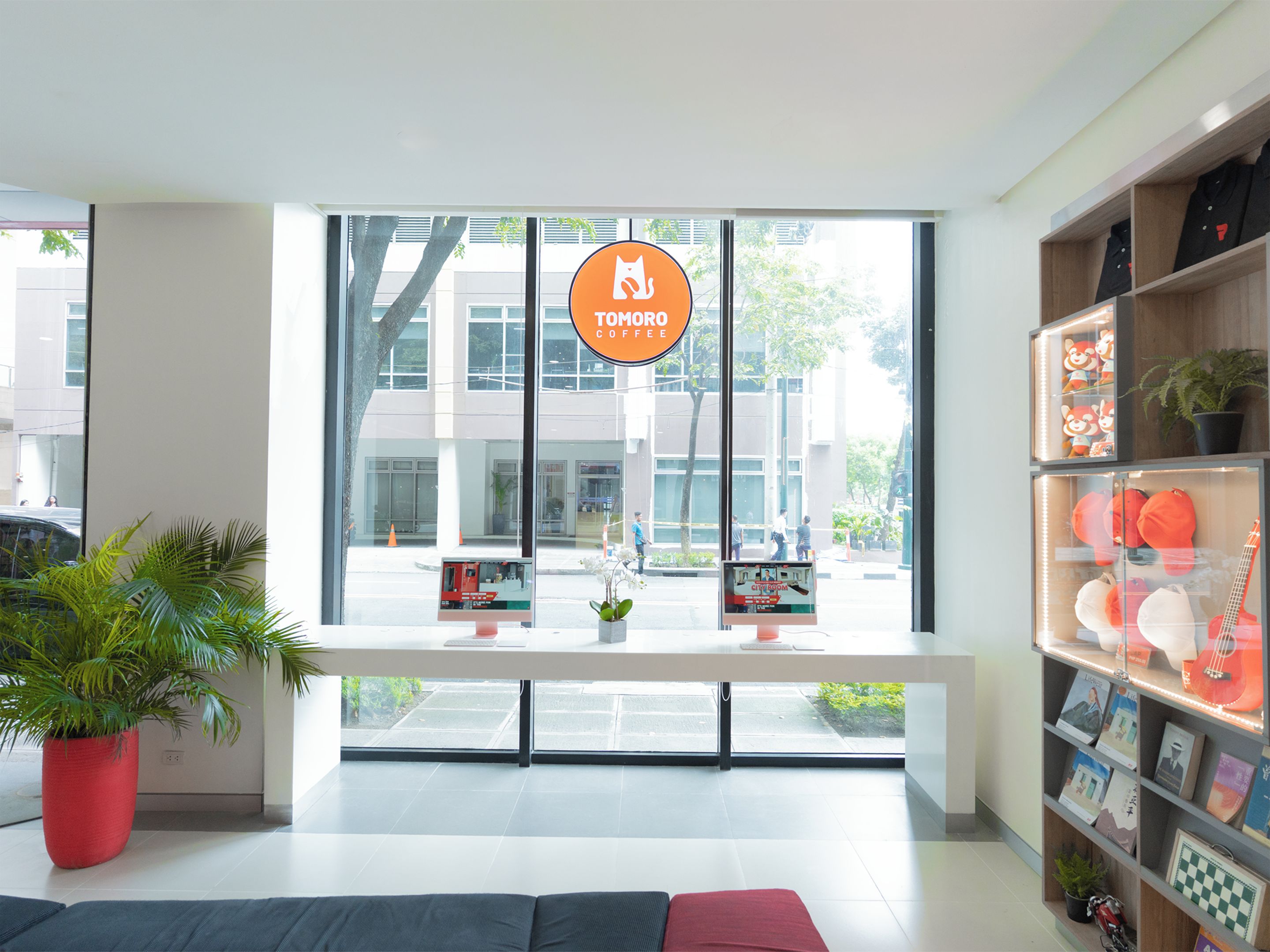 A modern interior with a large window, a red potted plant, and a bookshelf with various items.