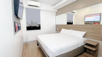 Quarto de hotel moderno com cama grande, televisão na parede, vista para a cidade e mesa de cabeceira de madeira.