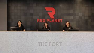 A reception desk with three staff members, a large 'R' logo, and the words 'RED PLANET' on the wall behind them.