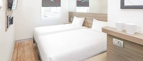 Une chambre d’hôtel avec un lit, une table de chevet sur laquelle sont posées deux tasses blanches, un miroir et une fenêtre donnant sur un panorama urbain.
