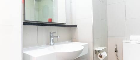 Un baño con lavamanos blanco, espejo, ducha e inodoro.