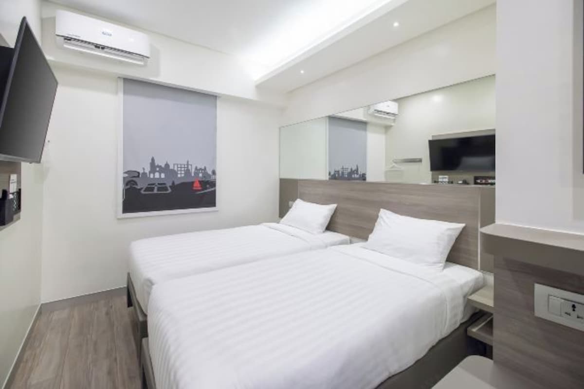 Habitación de hotel con dos camas, un televisor de pantalla plana, un cartel con una vista urbana y un espejo.