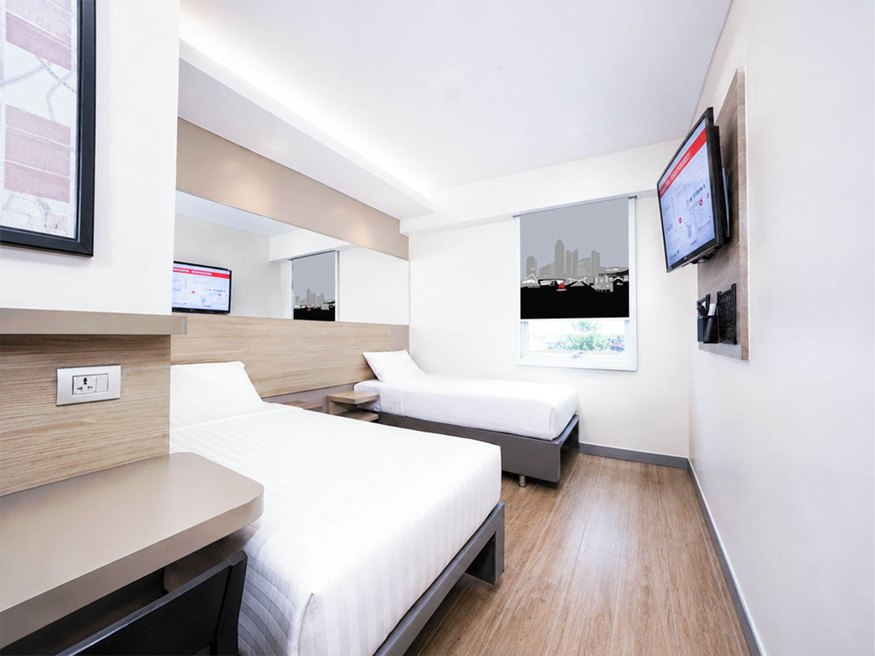 A hotel room with two beds, a desk, a TV, and a cityscape view.