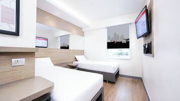 A hotel room with two beds, a desk, a TV, and a cityscape view.