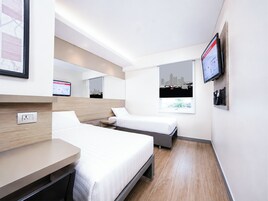 A hotel room with two beds, a desk, a TV, and a cityscape view.