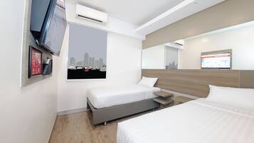 Una habitación de hotel moderna con dos camas, vistas a la ciudad, un equipo de aire acondicionado y un televisor montado.