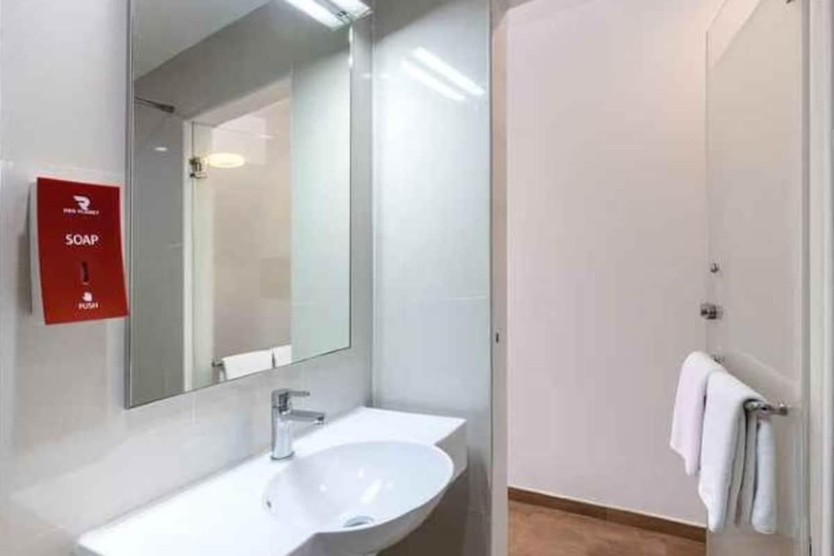 A modern bathroom with a white sink, a large mirror, and a red soap dispenser.