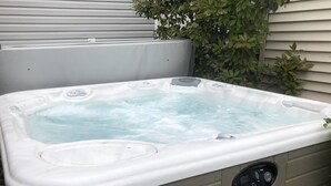Un jacuzzi con panel de control, frente a una pared color beige y un pequeño arbusto verde cercano.