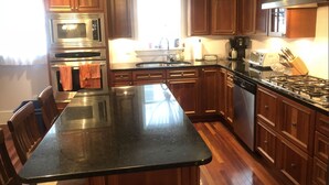 Una cocina con armarios de madera, electrodomésticos de acero inoxidable, una encimera negra y un ventanal que proporciona luz natural.