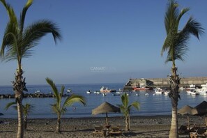 A beach with palm trees, a rocky shore, and boats in the water.
