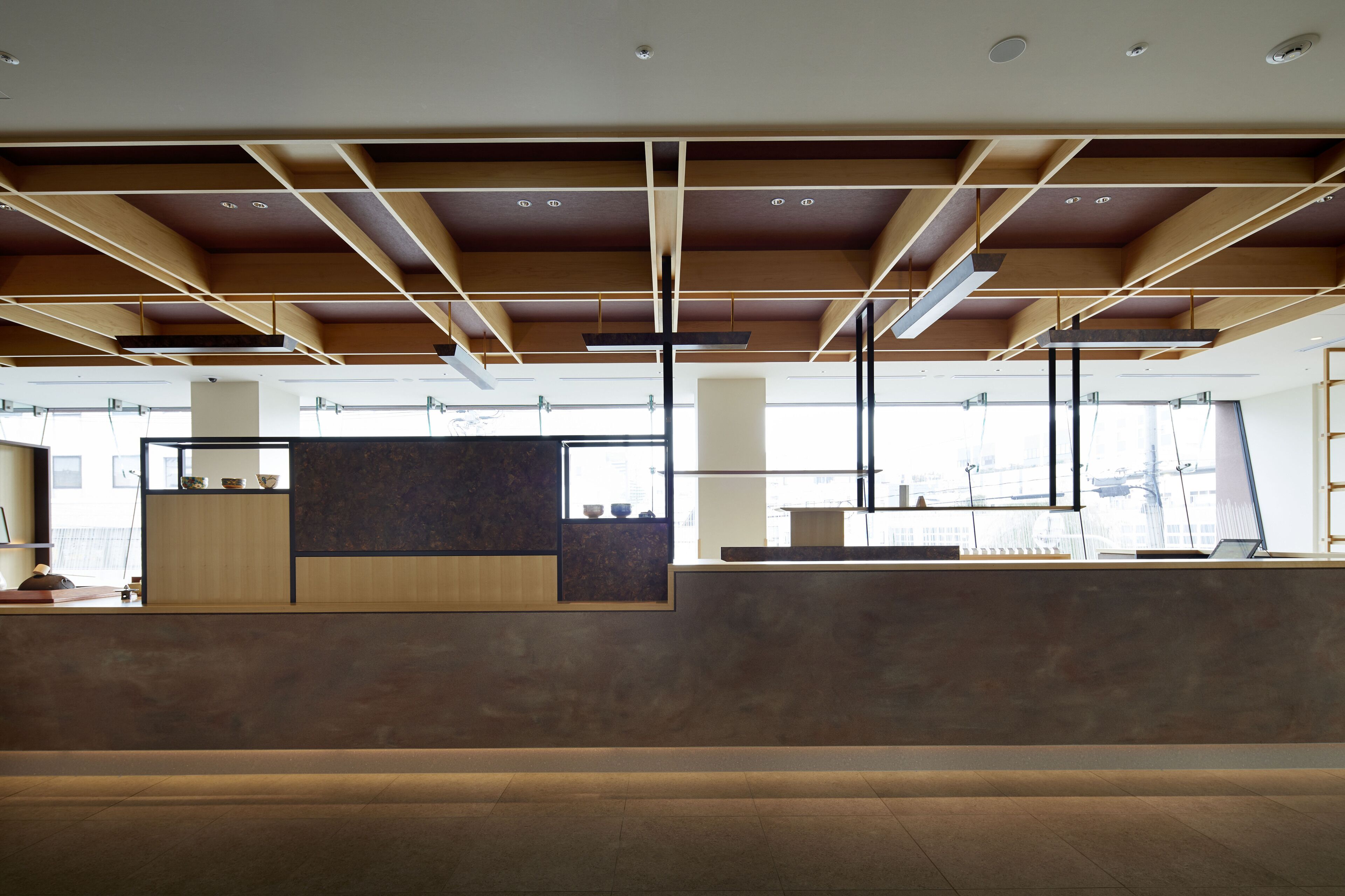 A modern interior with a reception desk, large windows, and a ceiling with exposed beams.